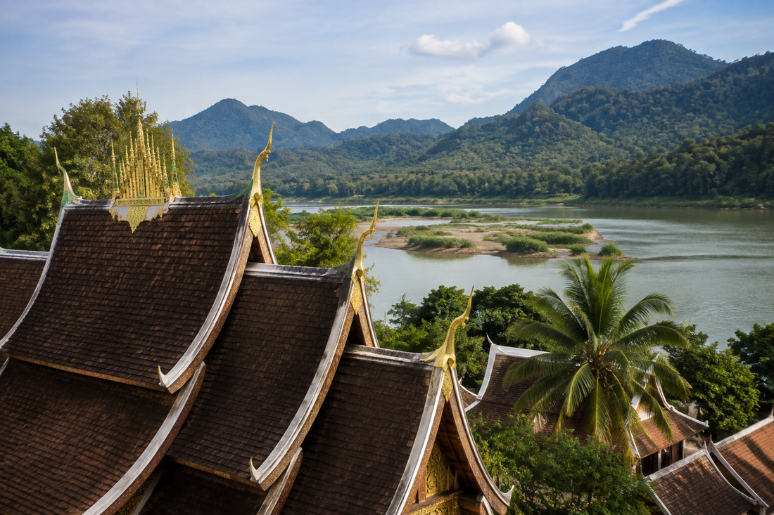 Illustrative Lao temple rooftops beside a river and green hills